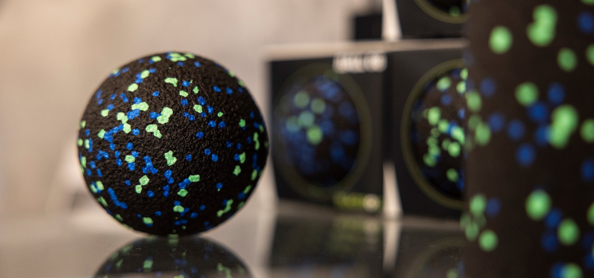 Therapiebälle zur Faszienbehandlung Verschiedene schwarze Therapiebälle mit bunten Punkten zur Faszienmassage auf einer Glasfläche präsentiert