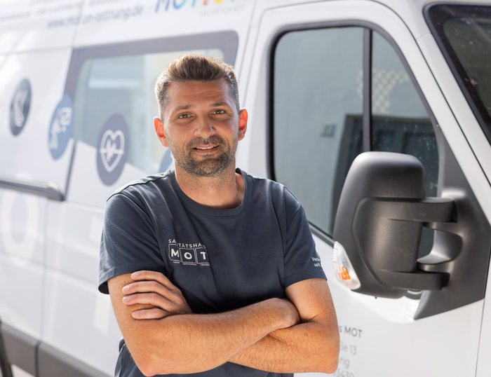 Ein freundlicher MOT-Mitarbeiter steht vor einem MOT-Lieferwagen
